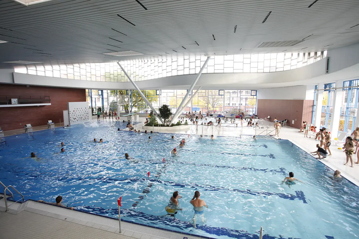 Blick in die Schwimmhalle auf das belebte Mehrzweckbecken und die geschwungene Dachkonstruktion im Leo-Vetter-Bad.