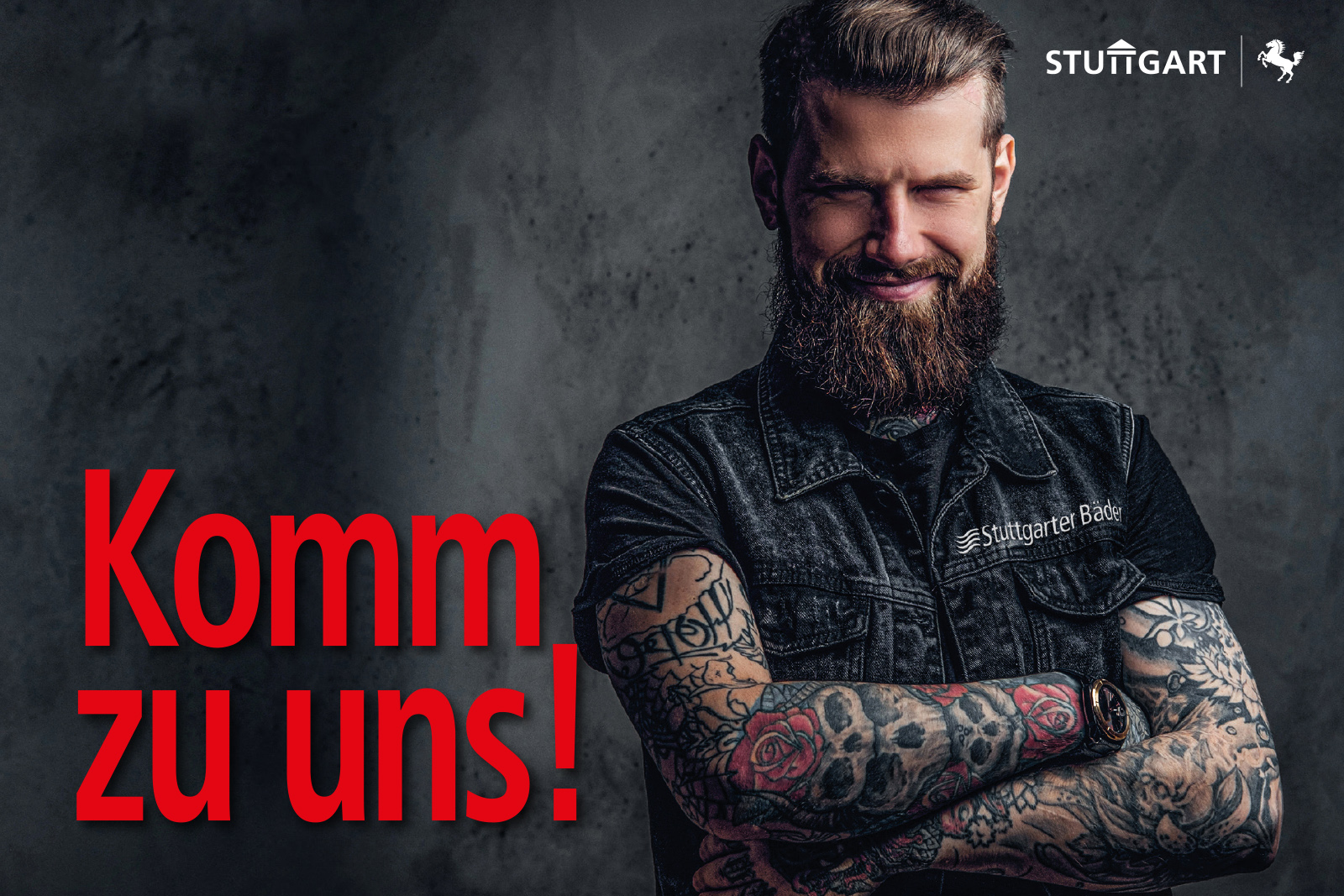 Auszubildendersuche: Ein tätovierter Mann/Rocker lächelt mit verschrenkten Armen in die Kamera.